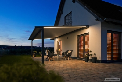 Weißes Haus mit Pergola Markise Warema P60 mit LED-Beleuchtung am Abend.